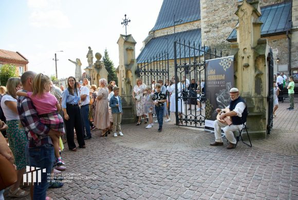 Grupa ludzi słucha muzyki i śpiewu lirnika.