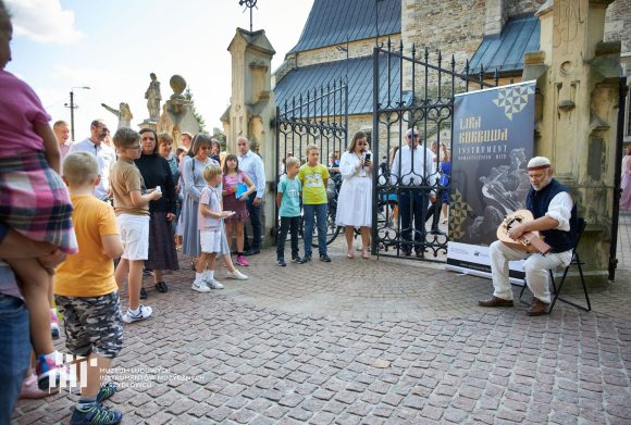 Grupa ludzi stoi i słucha muzyki granej przez lirnika.