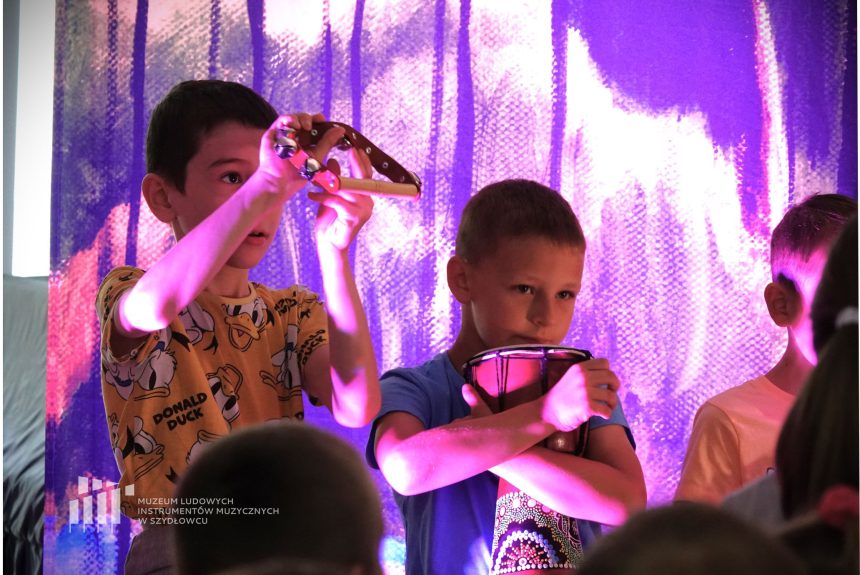 Dwóch chłopców trzyma w ręku instrumenty muzyczne. Tło w kolorze fioletowym.