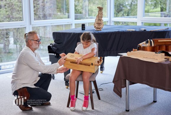 Mężczyzna w białej koszuli pomaga dziewczynce grać na instrumencie muzycznym.