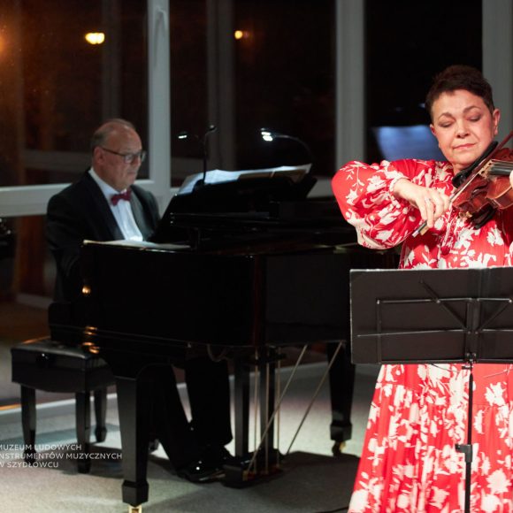 Zdjęcie skrzypaczki w czerwonej sukience i pianisty.