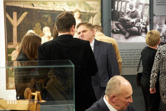 Zdjęcie. Dwóch mężczyzn rozmawia. Wokół nich znajdują się inni ludzie zwiedzający wystawę. Przodem Leszek Ruszczyk - dyrektor Muzeum im. Jacka Malczewskiego w Radomiu.