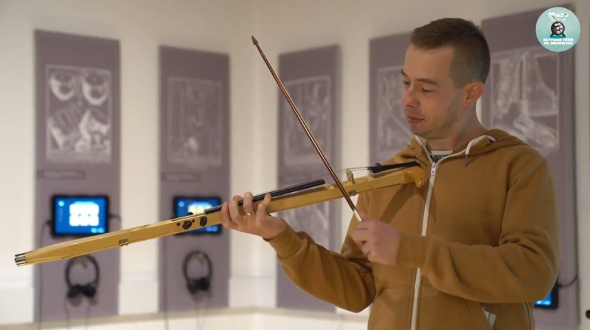 Zdjęcie. Młody mężczyzna w żółtej bluzie gra na skrzypcach laskowych.