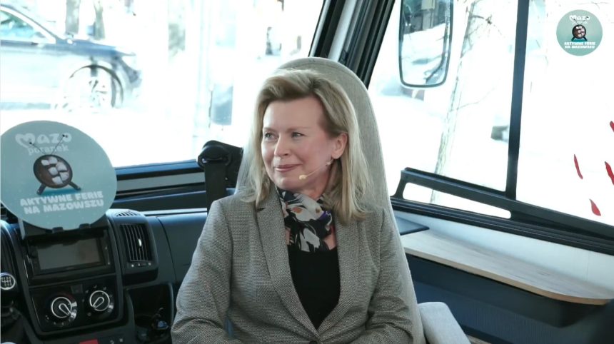 Zdjęcie. Uśmiechnięta kobieta w szarej marynarce siedzi w kabinie samochodu. Aneta Oborny dyrektor Muzeum Ludowych Instrumentów Muzycznych w Szydłowcu.