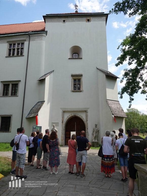 Grupa osób stojąca przed bramą do zamku w Szydłowcu