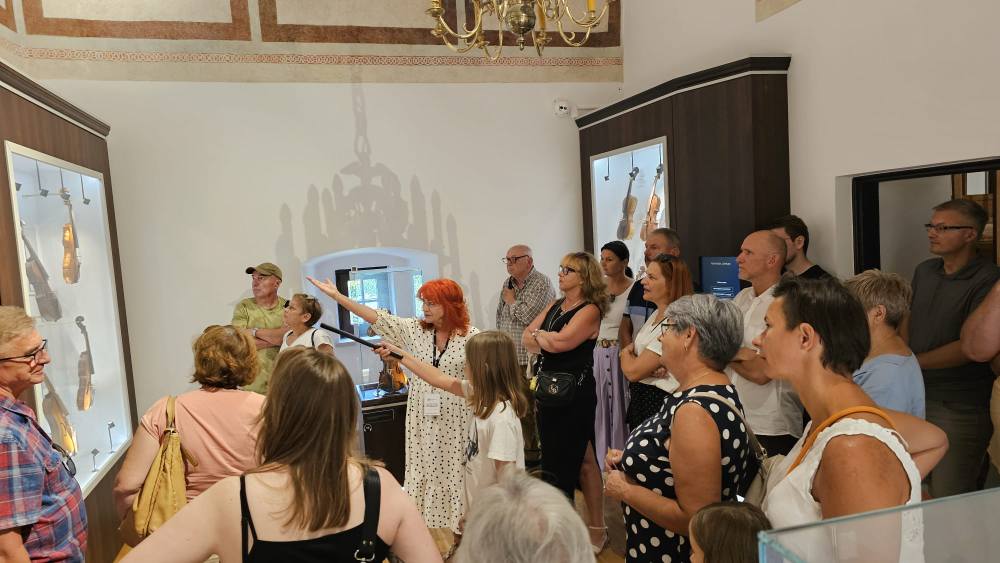 folkrelax_spacer_po_wystawach2 Grupa zwiedzających oraz dziewczynka uruchamiająca dźwięk instrumentów przy pomocy "batuty" i pomocą przewodnika w Komnacie Lutniczej.