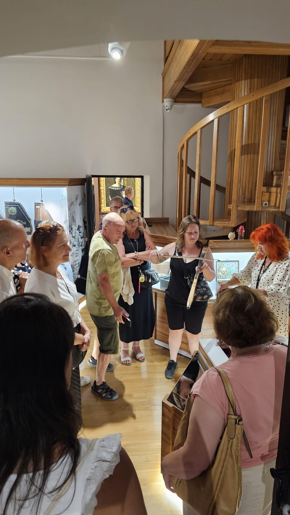 Grupa zwiedzających z przewodnikiem w Komnacie Intermezzo - Eksperymentarium Dźwięku przyglądająca się próbie grania na skrzypcach laskowych.