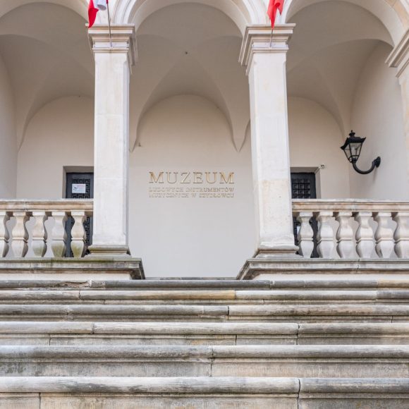 Zdjęcie. Na pierwszym planie szerokie, kamienne schody prowadzące pod arkady, w głębi wejście do muzeum.