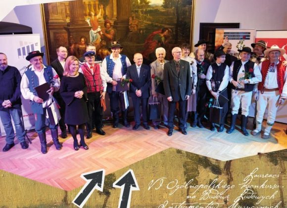 Zdjęcie. Grupa ludzi stojąca na scenie. Cześć z nich w strojach ludowych - laureaci VI Ogólnopolskiego Konkursu na Budowę Ludowych Instrumentów Muzycznych w 2022 roku