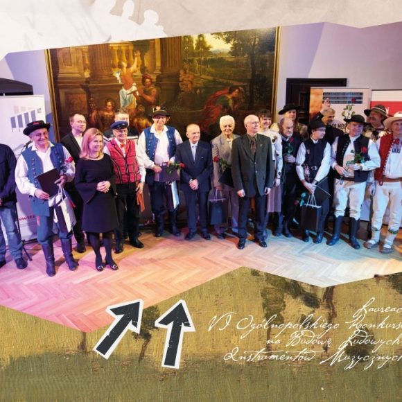 3-plansza_konkurs Grupa ludzi stojąca na scenie. Cześć z nich w strojach ludowych - laureaci VI Ogólnopolskiego Konkursu na Budowę Ludowych Instrumentów Muzycznych w 2022 roku