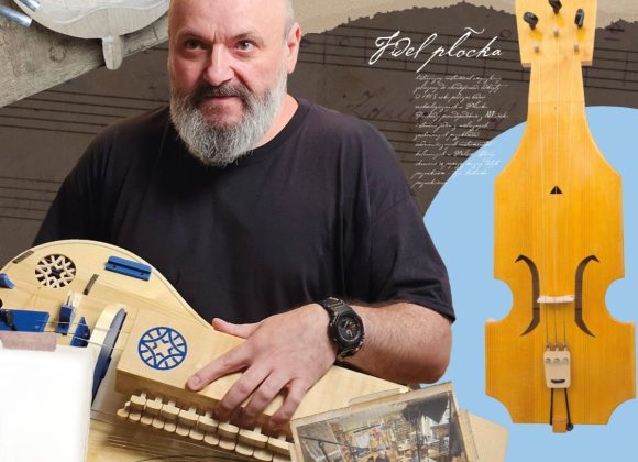 Zdjęcie. Mężczyzna bez włosów z brodą trzyma w rękach drewniany instrument - lirę korbową.