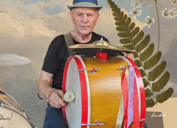 Zdjęcie. Mężczyzna w kapeluszu siedzi. Na kolanach trzyma duży bęben.