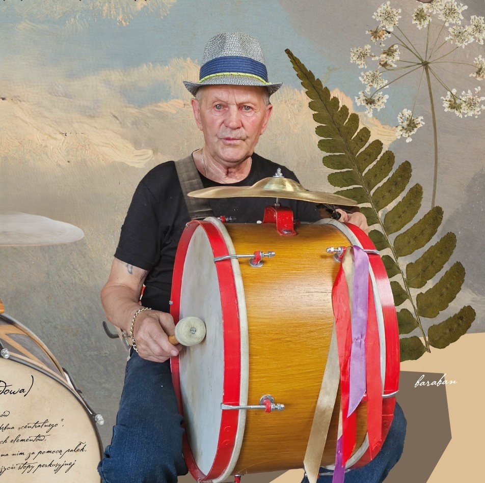 Zdjęcie. Mężczyzna w kapeluszu siedzi. Na kolanach trzyma duży bęben.