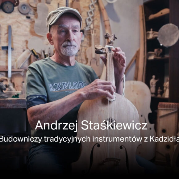 Na zdjęciu Andrzej Staśkiewicz w swojej pracowni gra na suce biłgorajskiej, którą sam zbudował. Za nim warsztat z narzędziami.
