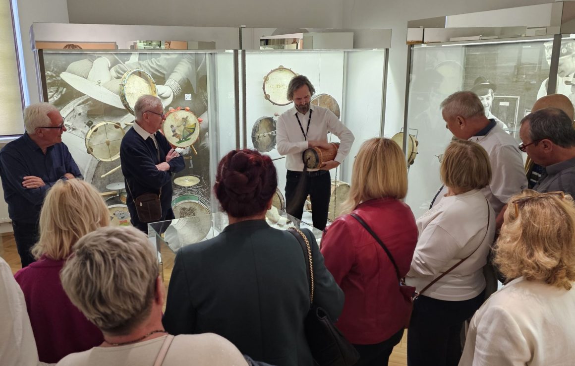 Senatorowie V kadencji Senatu Rzeczypospolitej wraz z przewodnikiem w Eksperymentarium Dźwięku podczas oprowadzania po wystawach w Muzeum Ludowych Instrumentów Muzycznych w Szydłowcu. Przewodnik prezentuje zwiedzającym grę na burczybasie.