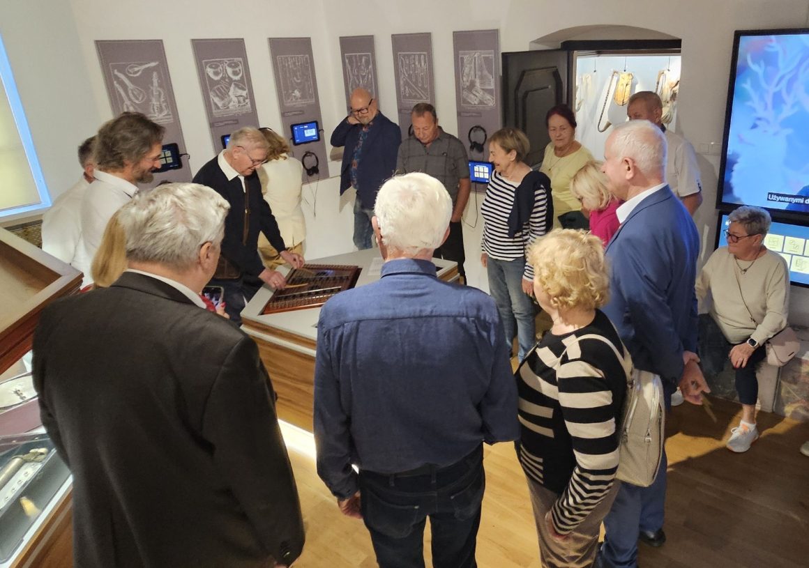 Senatorowie V kadencji Senatu Rzeczypospolitej wraz z przewodnikiem w Eksperymentarium Dźwięku podczas oprowadzania po wystawach w Muzeum Ludowych Instrumentów Muzycznych w Szydłowcu. Jeden z uczestników próbuje grać na cymbałach.