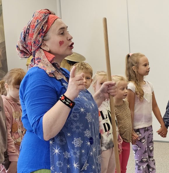 Aktorka z teatrzyku „Słuchaj uchem” oraz dziecięca publiczność podczas spektaklu „Kusy Janek”. Dzieci uczestniczą w zabawie tanecznej.