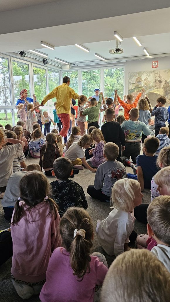 Aktorzy z teatrzyku „Słuchaj uchem” oraz dziecięca publiczność podczas spektaklu „Kusy Janek”. Część dzieci uczestniczy w zabawie tanecznej, reszta siedzi i ogląda spektakl.