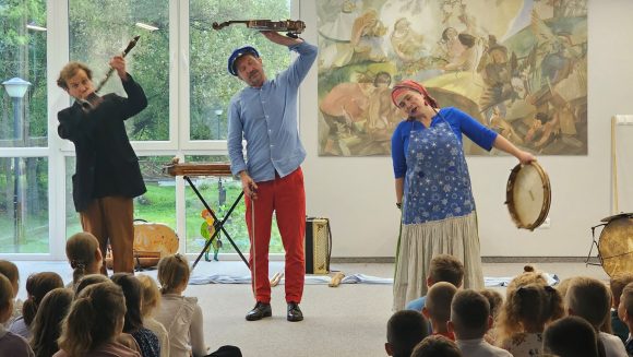 Aktorzy z teatrzyku „Słuchaj uchem” grający na skrzypcach, klarnecie i bębenku oraz dziecięca publiczność podczas spektaklu „Kusy Janek”.