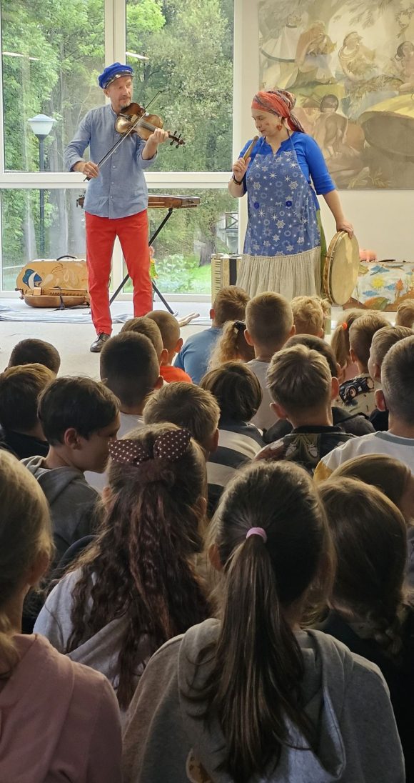 Aktorzy z teatrzyku „Słuchaj uchem” grający na skrzypcach i bębenku oraz dziecięca publiczność podczas spektaklu „Kusy Janek”.