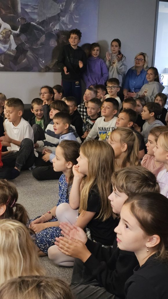 Dziecięca publiczność podczas spektaklu „Kusy Janek”. Część dzieci uczestniczy w zabawie tanecznej, reszta siedzi i ogląda spektakl.