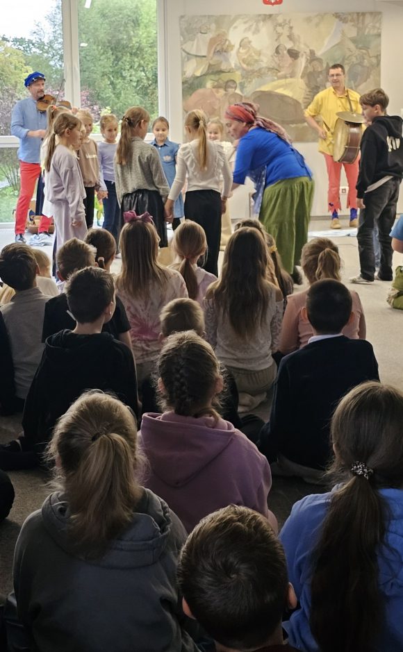 Aktorzy z teatrzyku „Słuchaj uchem” oraz dziecięca publiczność podczas spektaklu „Kusy Janek”. Część dzieci uczestniczy w zabawie tanecznej, reszta siedzi i ogląda spektakl.