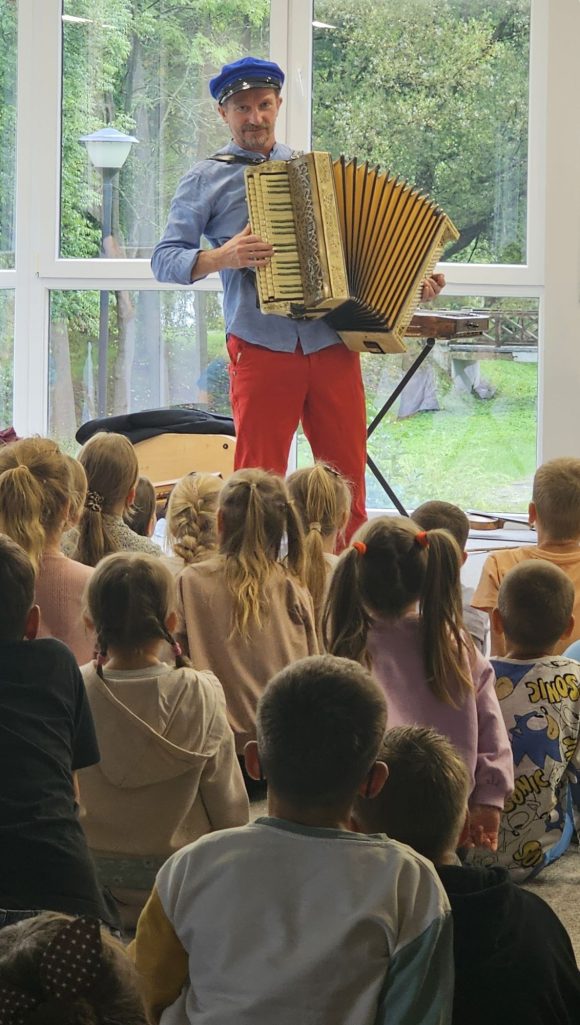 Aktor z teatrzyku „Słuchaj uchem” prezentujące akordeon oraz dziecięca publiczność podczas spektaklu „Kusy Janek”.