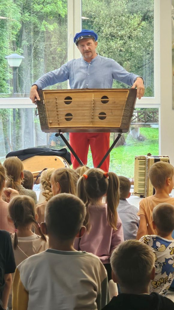 Aktor z teatrzyku „Słuchaj uchem” prezentujący cymbały oraz dziecięca publiczność podczas spektaklu „Kusy Janek”.