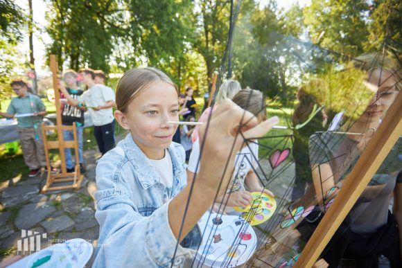 Na pierwszym planie uczniowie Publicznej Szkoły Podstawowej nr 2 im. Jana Pawła II w Szydłowcu podczas zajęć artystycznych „Witraż w plenerze”.