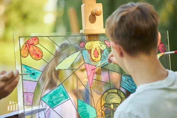 Na pierwszym planie uczniowie Publicznej Szkoły Podstawowej nr 2 im. Jana Pawła II w Szydłowcu podczas zajęć artystycznych „Witraż w plenerze”.