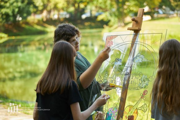 Na pierwszym planie uczniowie Publicznej Szkoły Podstawowej nr 2 im. Jana Pawła II w Szydłowcu podczas zajęć artystycznych „Witraż w plenerze”.