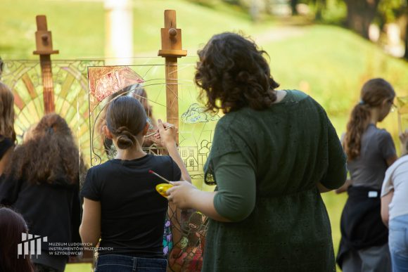 Na pierwszym planie uczniowie Publicznej Szkoły Podstawowej nr 2 im. Jana Pawła II w Szydłowcu podczas zajęć artystycznych „Witraż w plenerze”. W tle park przy zamku.