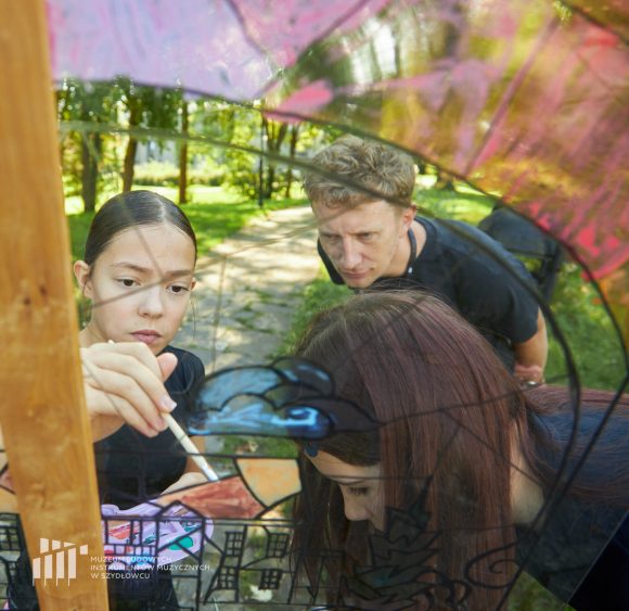 Na pierwszym planie uczniowie Publicznej Szkoły Podstawowej nr 2 im. Jana Pawła II w Szydłowcu oraz pracownik muzeum podczas zajęć artystycznych „Witraż w plenerze”.