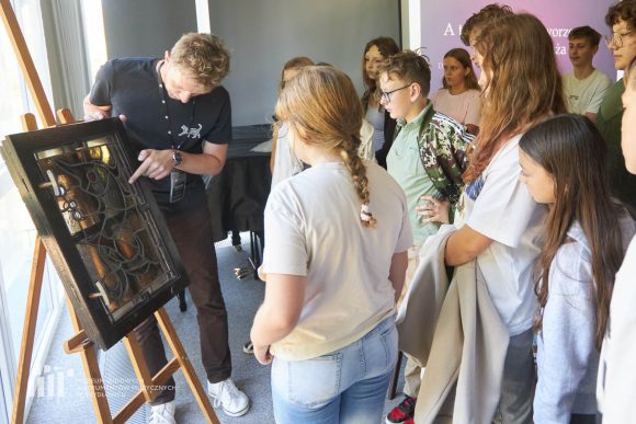 Prezentacja witrażu przez prowadzącego prelekcję oraz uczniowie Publicznej Szkoły Podstawowej nr 2 im. Jana Pawła II w Szydłowcu podczas zajęć artystycznych „Witraż w plenerze”.