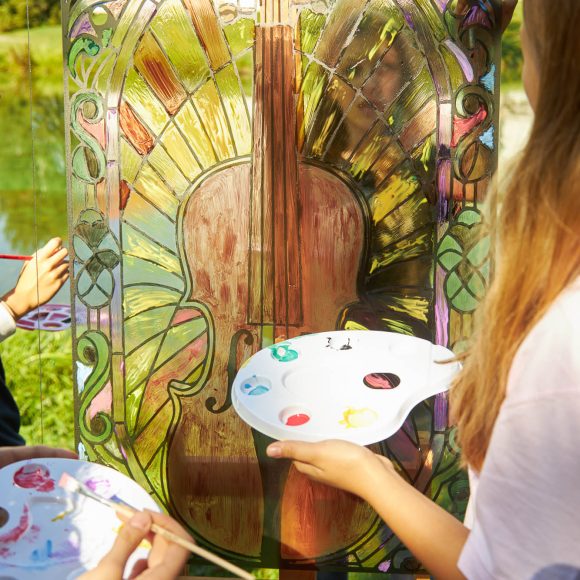 witraż w plenerze Na pierwszym planie uczniowie Publicznej Szkoły Podstawowej nr 2 im. Jana Pawła II w Szydłowcu podczas zajęć artystycznych „Witraż w plenerze”. W tle fosa i fragment zamku.