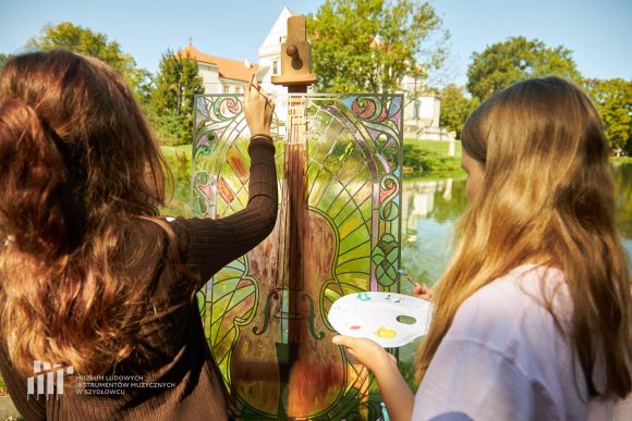 Na pierwszym planie uczniowie Publicznej Szkoły Podstawowej nr 2 im. Jana Pawła II w Szydłowcu podczas zajęć artystycznych „Witraż w plenerze”. W tle fosa i fragment zamku.