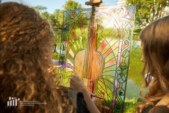 Na pierwszym planie uczniowie Publicznej Szkoły Podstawowej nr 2 im. Jana Pawła II w Szydłowcu podczas zajęć artystycznych „Witraż w plenerze”. W tle fosa przy zamku.