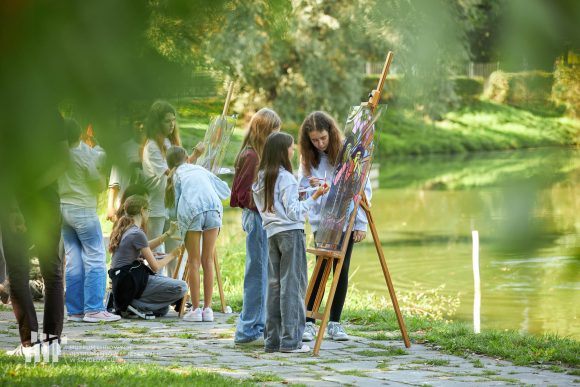Na pierwszym planie uczniowie Publicznej Szkoły Podstawowej nr 2 im. Jana Pawła II w Szydłowcu podczas zajęć artystycznych „Witraż w plenerze”. W tle fosa przy zamku.
