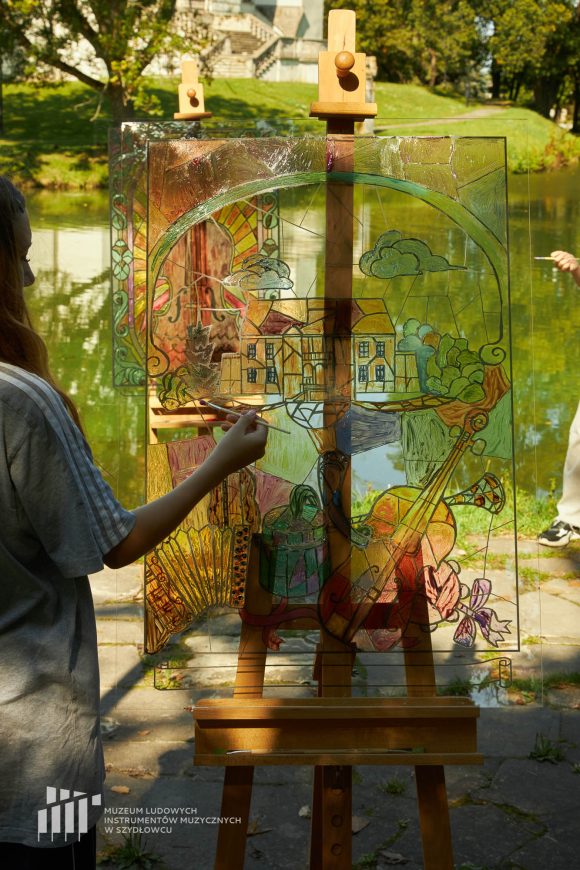 Na pierwszym planie uczennica Publicznej Szkoły Podstawowej nr 2 im. Jana Pawła II w Szydłowcu podczas zajęć artystycznych „Witraż w plenerze”. W tle fosa i fragment zamku.