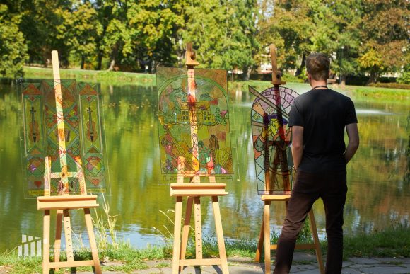 Na pierwszym planie oglądający efekt pracy uczniów Publicznej Szkoły Podstawowej nr 2 im. Jana Pawła II w Szydłowcu podczas zajęć artystycznych „Witraż w plenerze”. W tle fosa przy zamku.