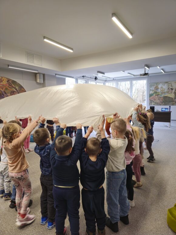 Dzieci poruszają płachtę foliową tworząc fale.