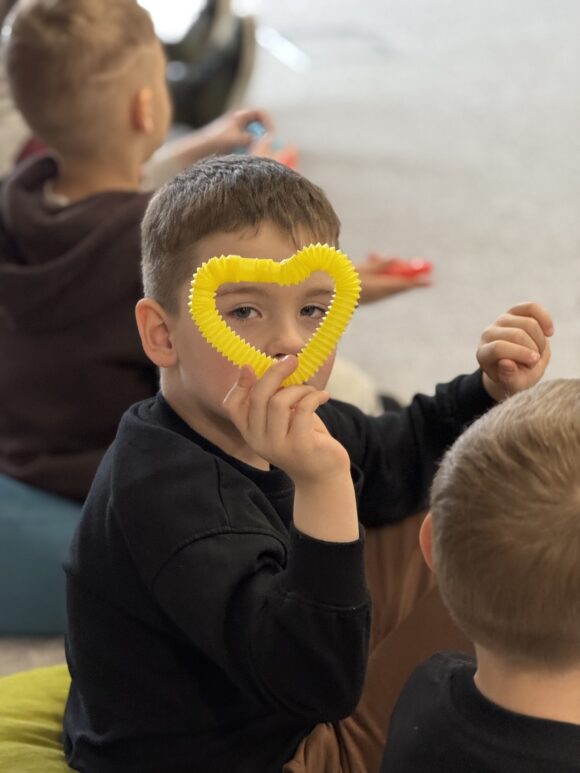 Chłopiec trzyma przy twarzy żółte serce zrobione z długiej, sprężystej rurki.